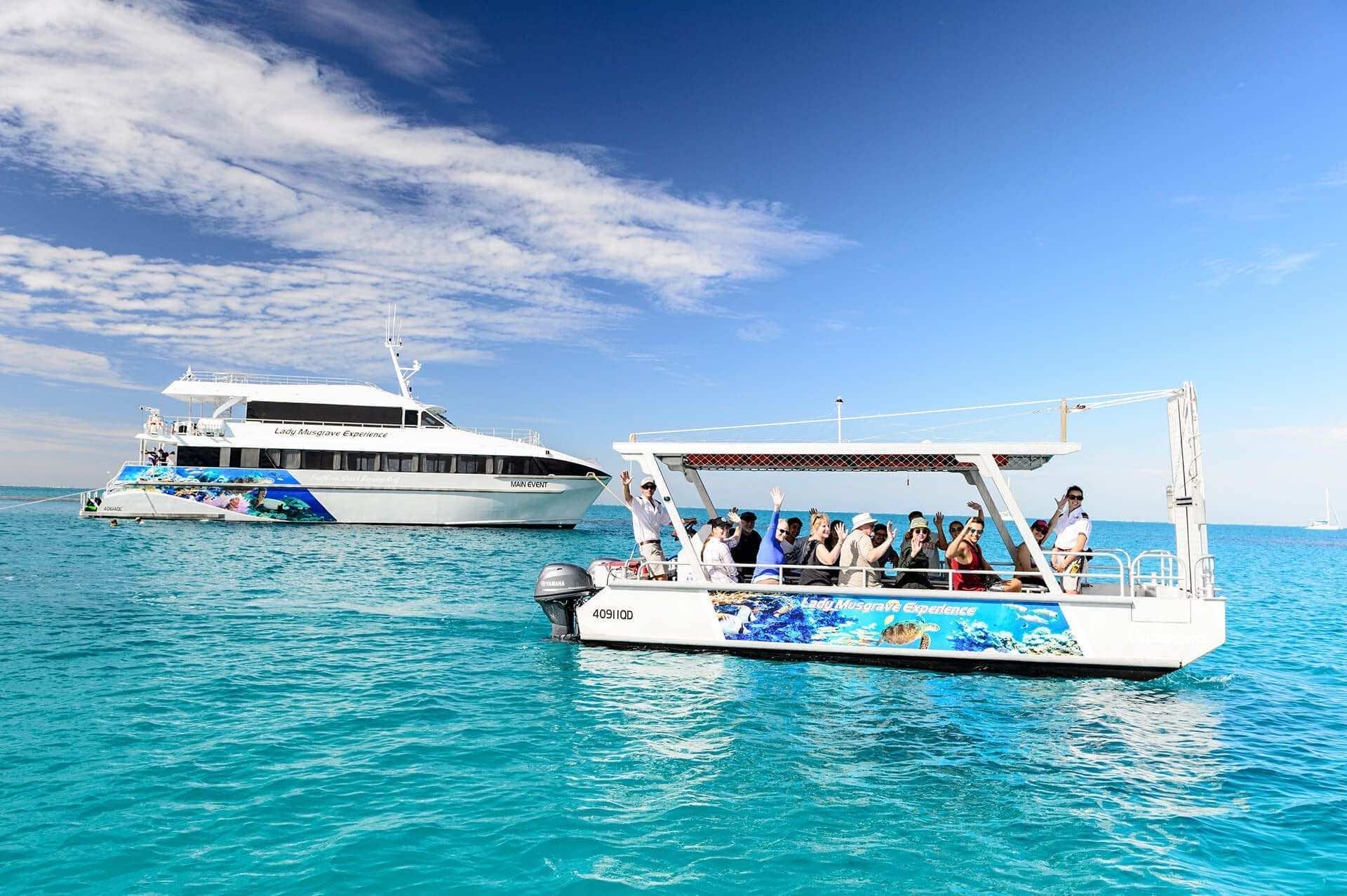 Guests waving from the reef tender beside the Main Event vessel in the Lady Musgrave Island lagoon